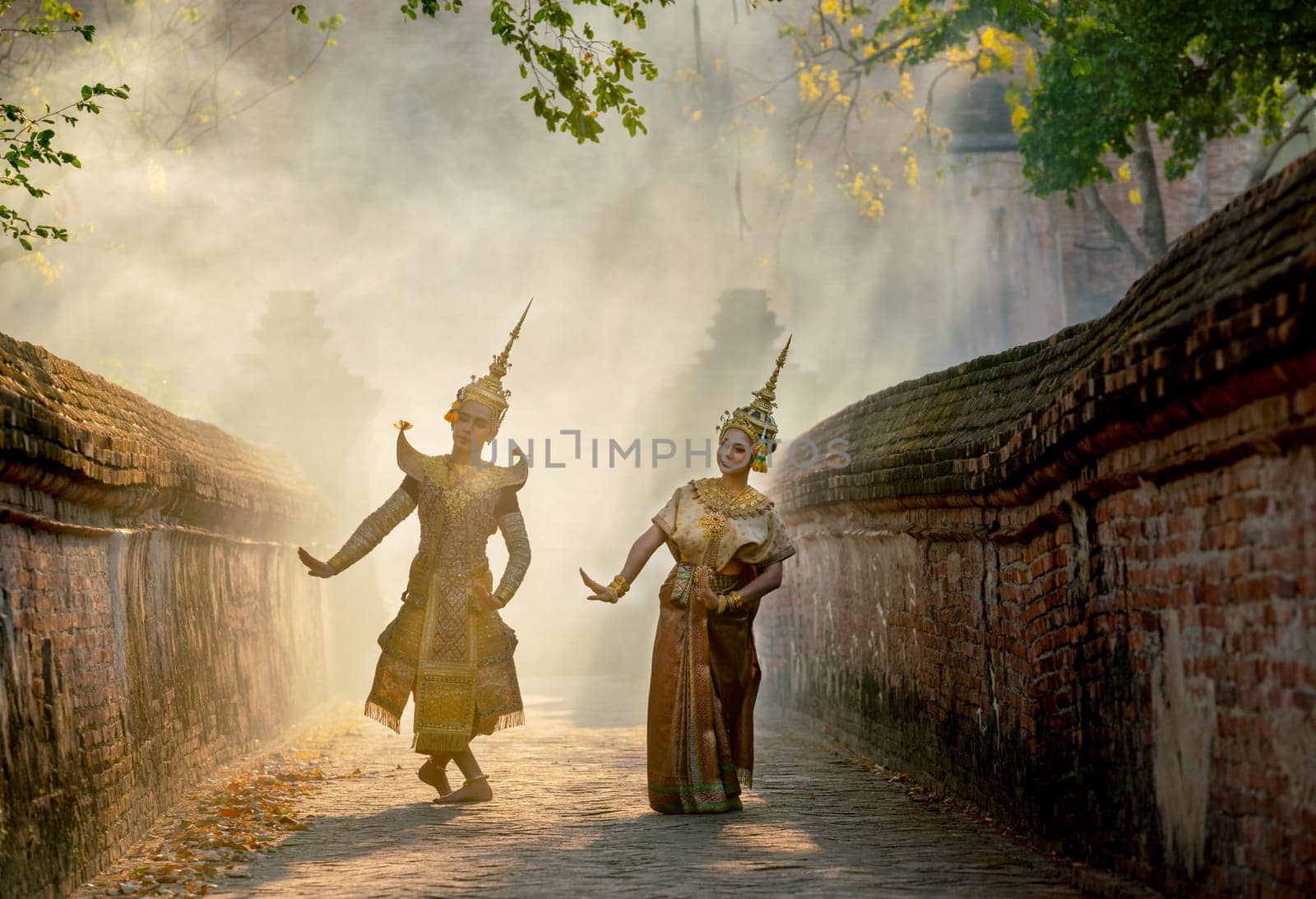 Asian man and woman wear Thai traditional dress and dance with beautifuul cultural style on the way with ancient wall and building in background.