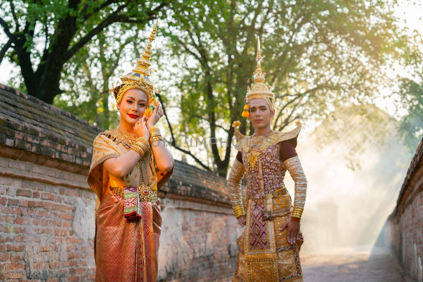 Portrait of Asian man and woman with Thai traditional dress stand together in front of ancient wall and building.