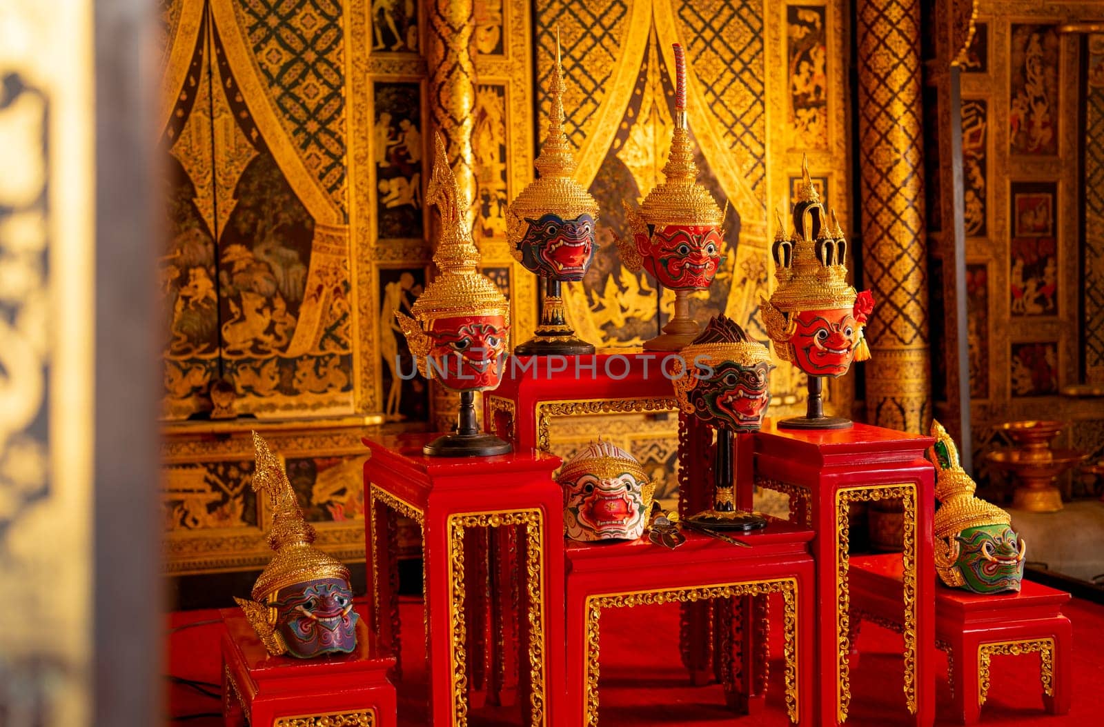 Side view of beautiful ancient traditional Thai pattern Pantomime or Khon masks are set up on wooden shelves with Thai painting as background of public place in Thailand.