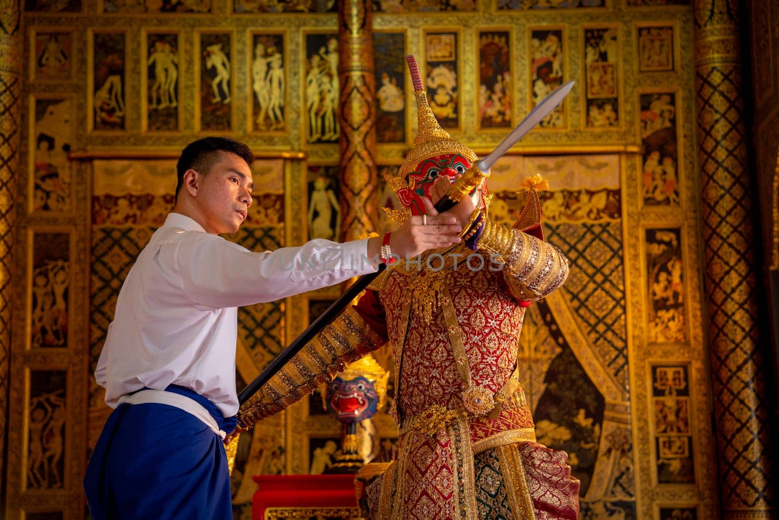 Close up Asian man with Thai style cloth action of teaching to man wear ancient traditional Thai pattern Pantomime in room with Thai painting style on wall of public place.