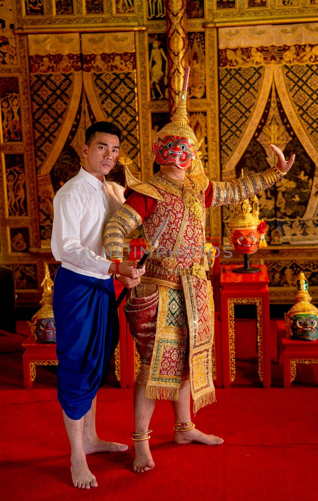 Asian man with Thai style cloth action of teaching to man wear ancient traditional Thai pattern Pantomime in room with Thai painting style on wall of public place.