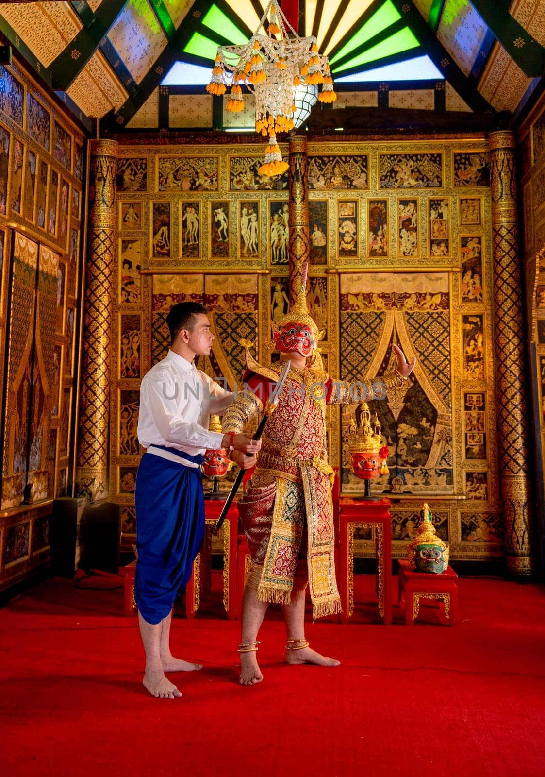 Asian man with Thai style cloth action of teaching to man wear ancient traditional Thai pattern Pantomime in room with Thai painting style on wall of public place.