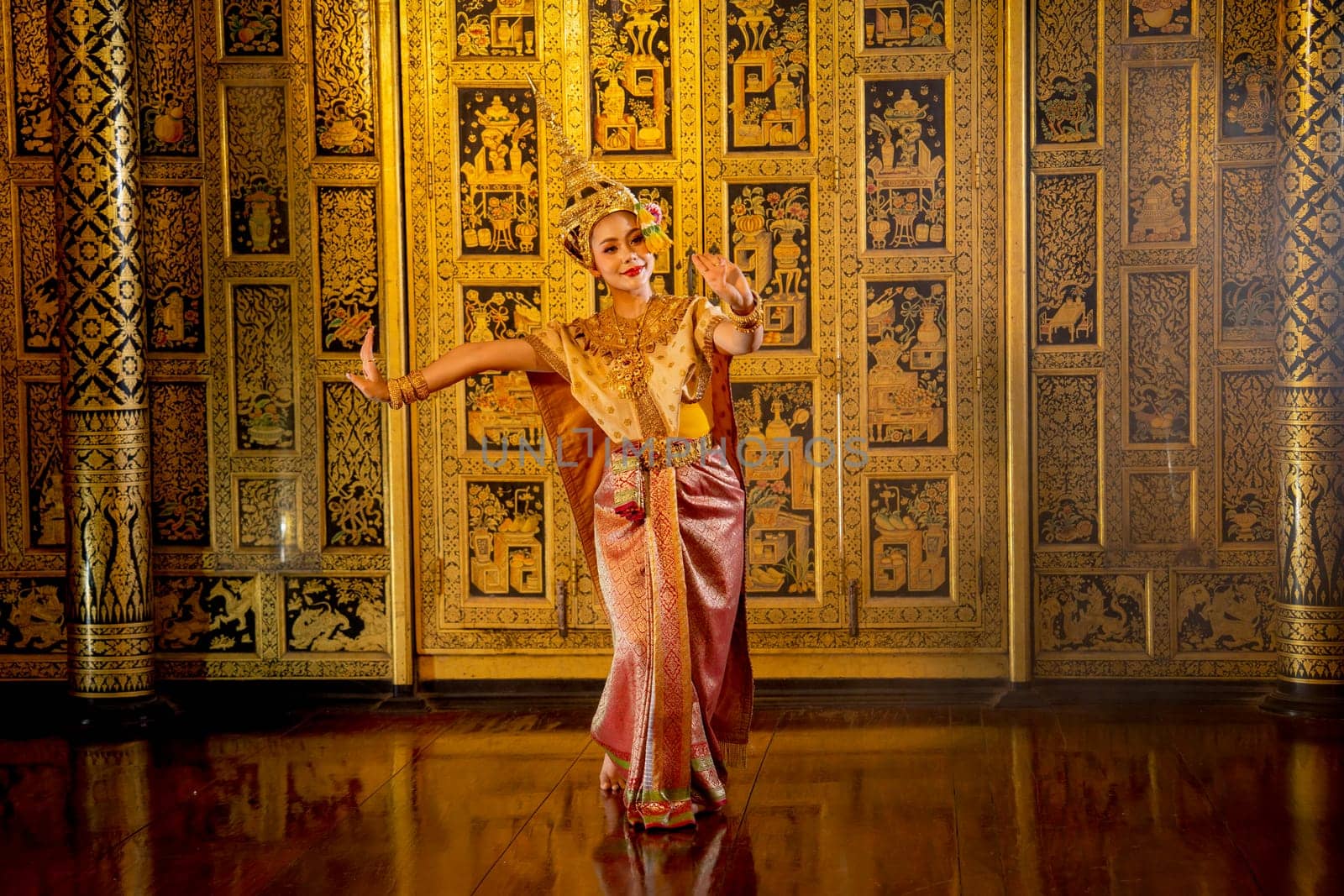 Wide shot of beautiful Asian woman wear Thai ancient traditional dress action of dancing in front of Thai painting as background in public place.