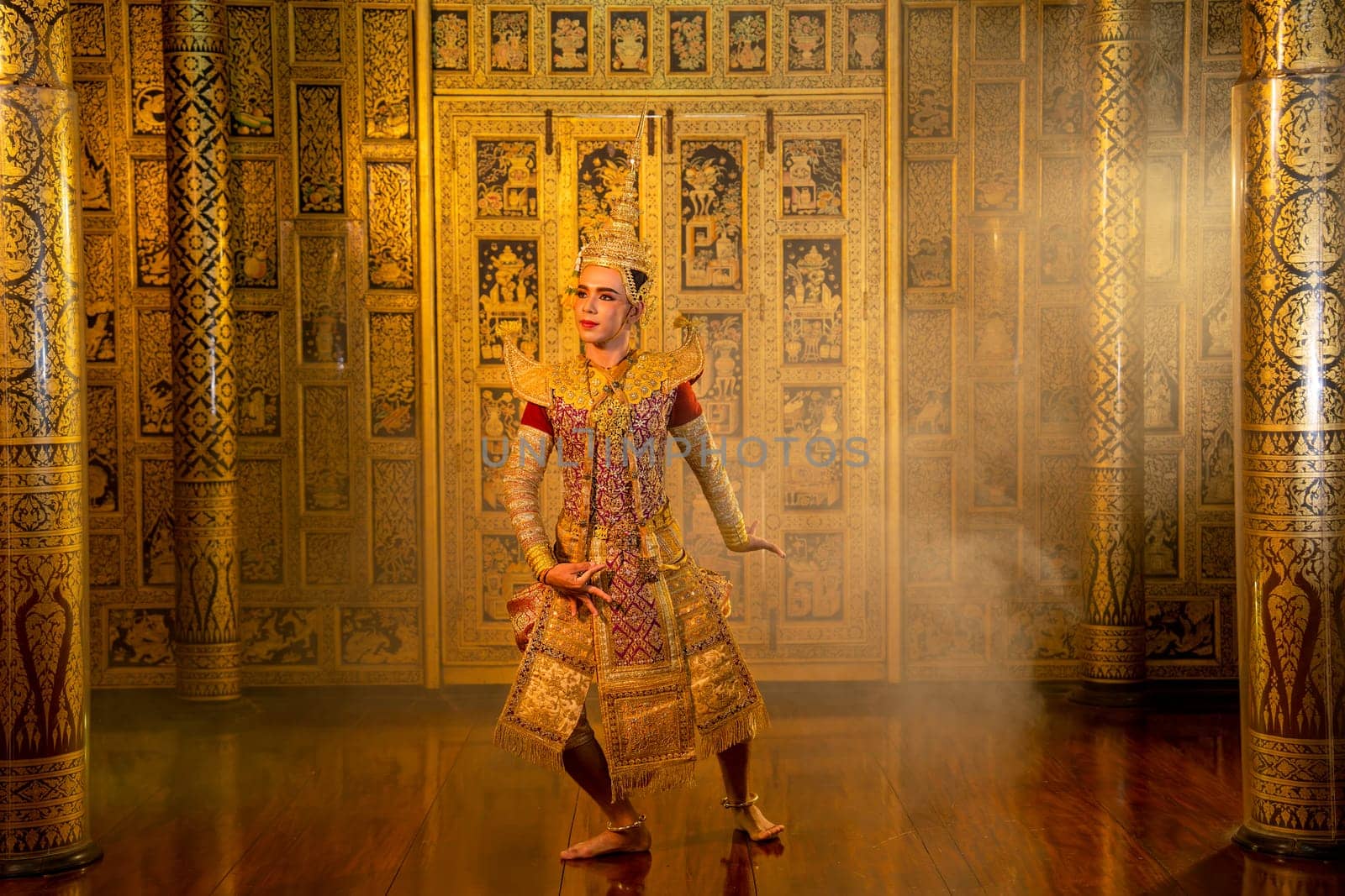 Asian man with Thai traditional cloth dance show in front of Thai painting on wall of public place.