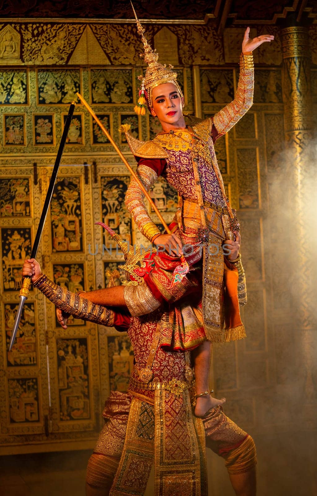 Vertical image of Khon or traditional Thai classic masked from the Ramakien characters action of traditional dance with fighting between human and giant with Thai painting on the wall in background.