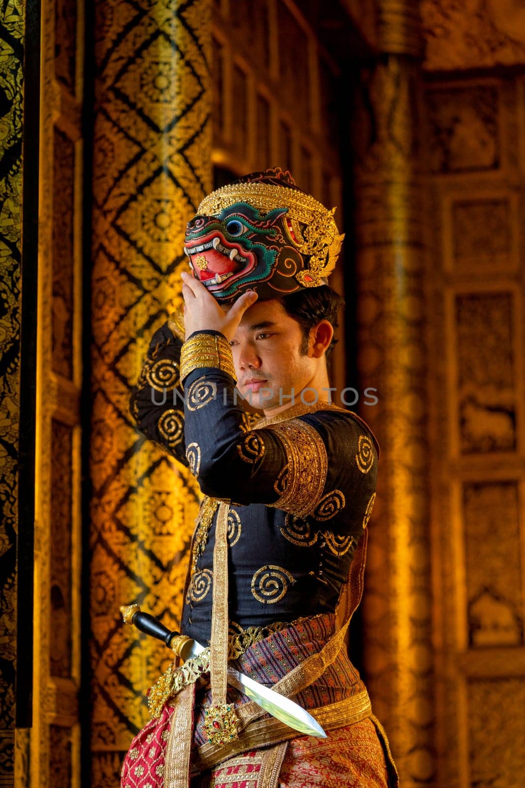 Vertical image of Asian man with traditional cloth relate to Khon or Thai classic masked with holding black monkey mask stand in front of windows of public building.