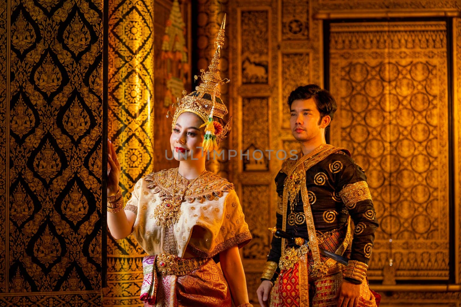 Beautiful Asian woman with Thai traditional dress stand in front of windows and look outside also Asian man with black traditional dress in the back.