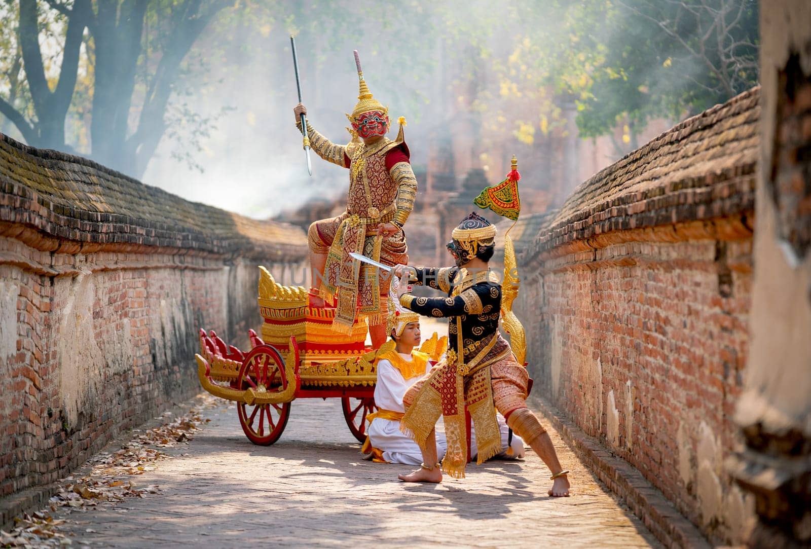 Khon or traditional Thai classic masked as character of red giant stand on traditional chariot also fight to black monkey with stay in front of ancient building with mist or fog.