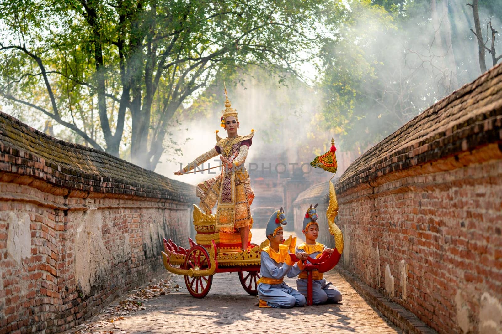 Asian man with old Thai traditional cloth hold weapon and stand and action of dance on traditional chariot also hold weapon stay in front of ancient building.