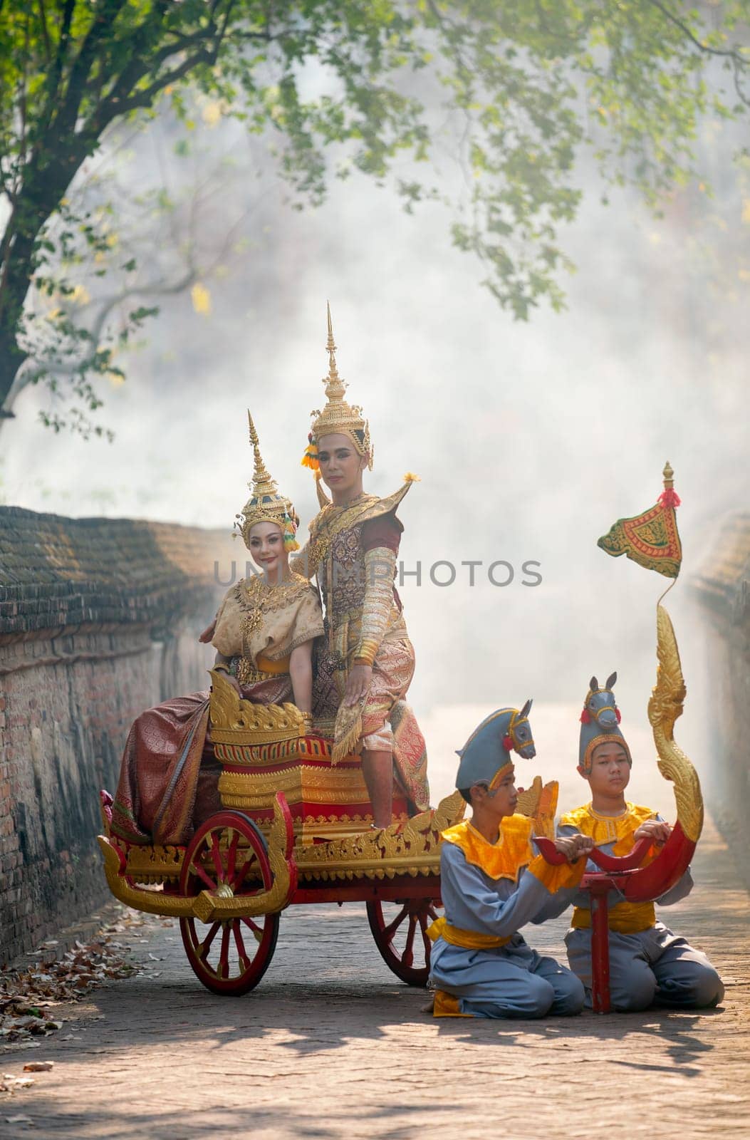 Asian man and woman with Thai old traditional dress stay together on traditional chariot in front of ancient building.