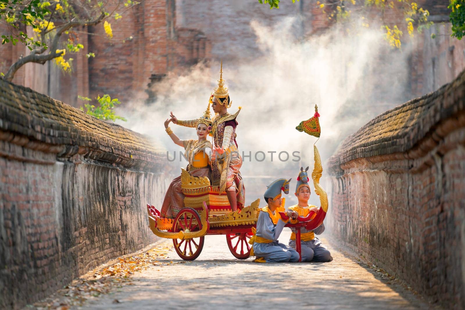 Asian man and woman with Thai old traditional dress stay together on traditional chariot in front of ancient building.