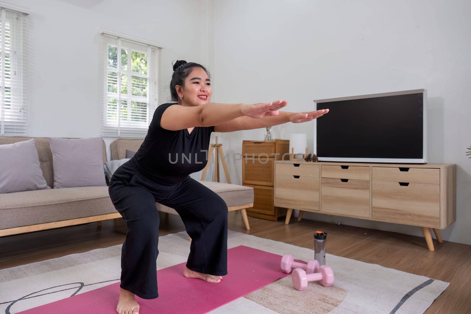 Fat woman exercising at home A beautiful oversized woman in a sports bra and casual pants stands in the living room and exercises..