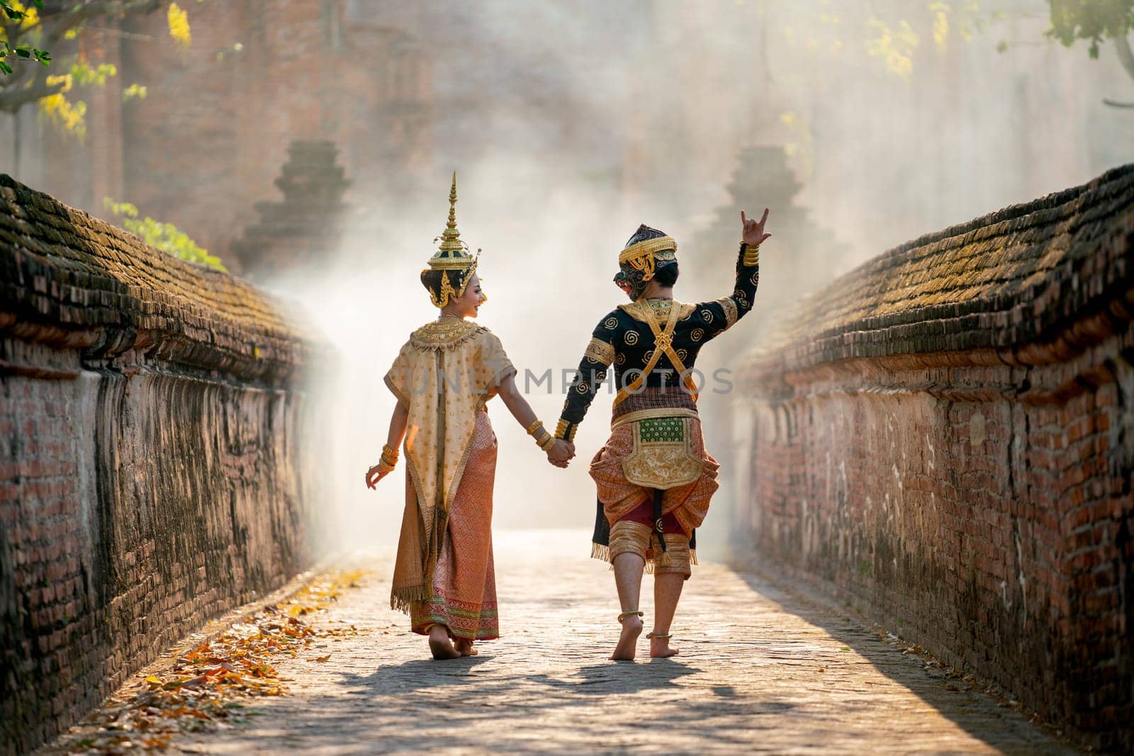 Asian woman wear Thai traditional dress action of walking with holdin hand with Thai classic masked from the Ramakien character as black monkey with ancient wall and buildin in backgground.