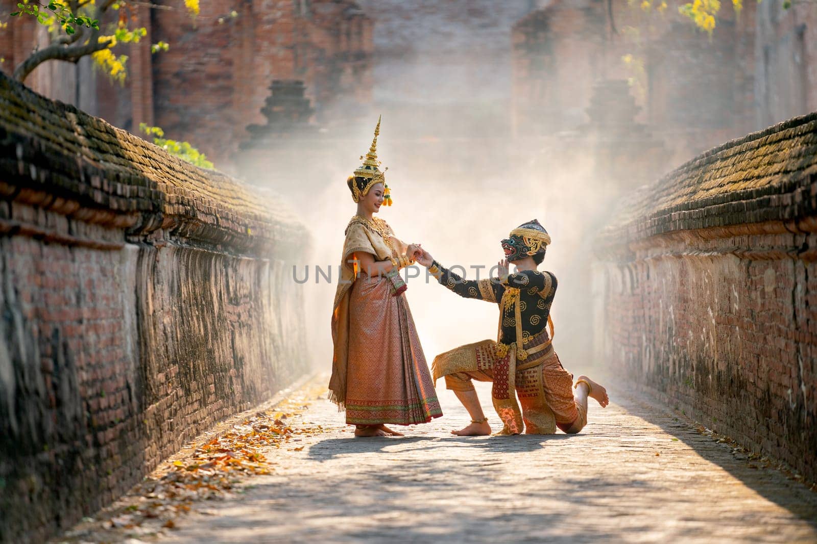 Beautiful Asian woman wear Thai traditional dress stand together with Thai classic masked from the Ramakien as black monkey sit on floor with ancient wall and buildin in backgground.