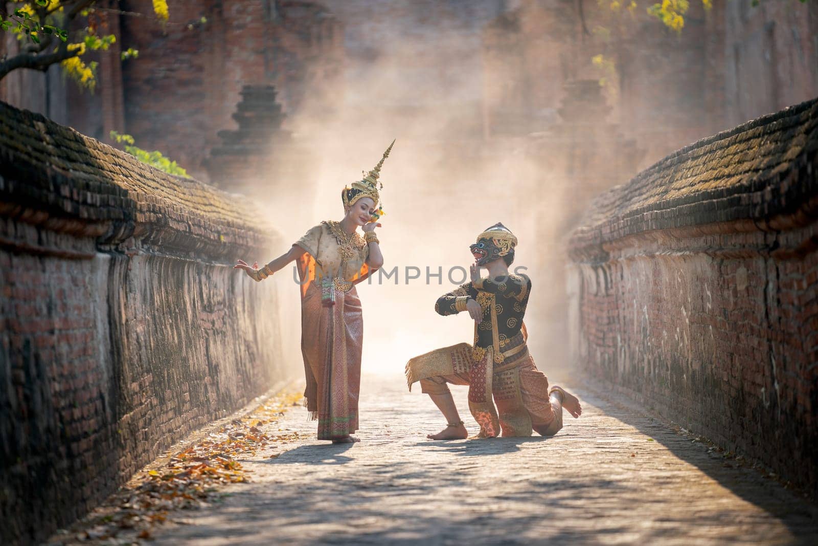 Beautiful Asian woman wear Thai traditional dress action of dancing together with Thai classic masked from the Ramakien character as black monkey with ancient wall and buildin in backgground.