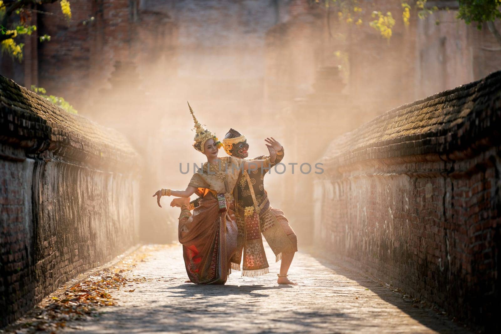 Beautiful Asian woman wear Thai traditional dress action of dancing together with Thai classic masked from the Ramakien character as black monkey with ancient wall and buildin in mist background.