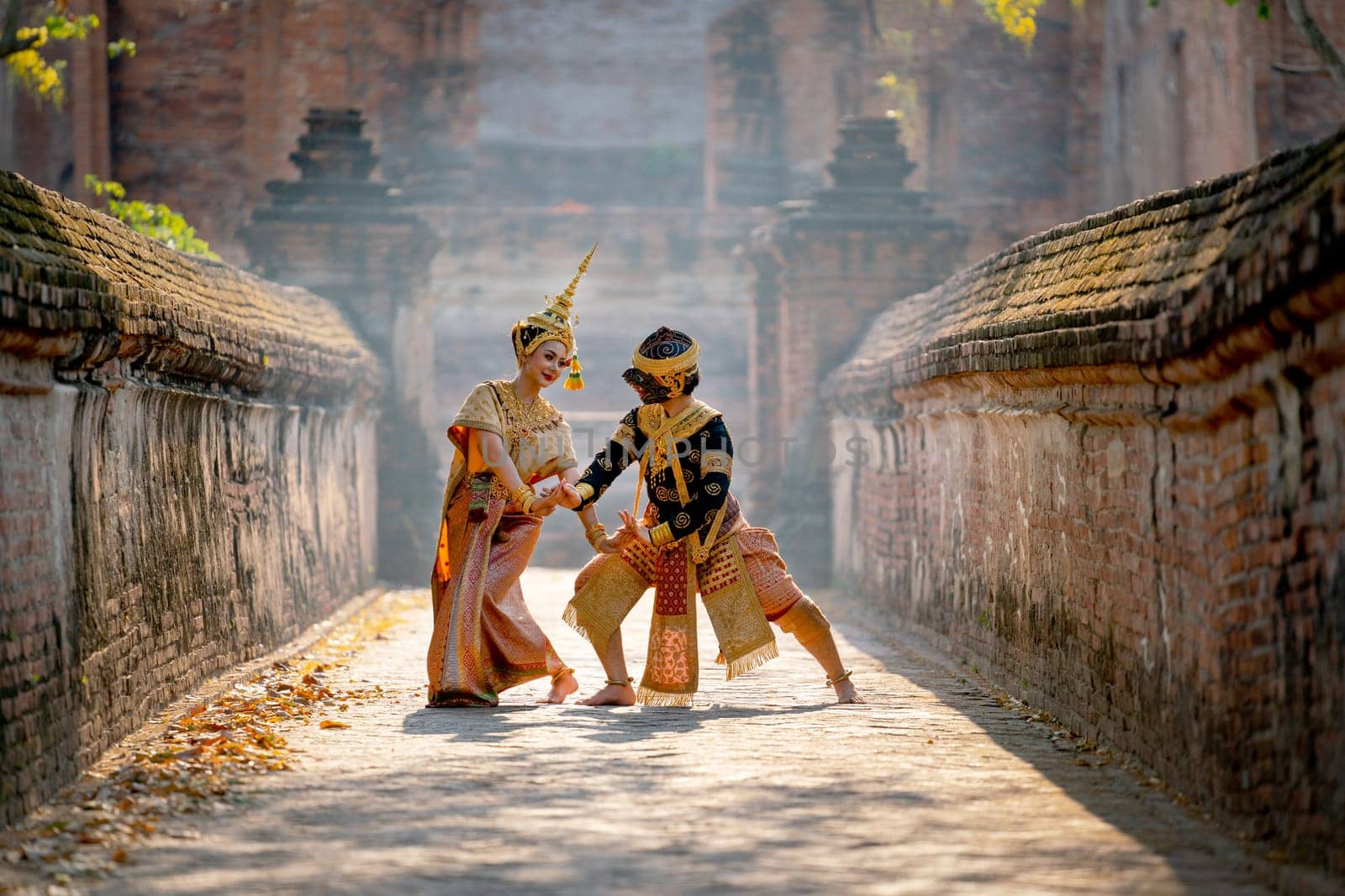 Beautiful Asian woman wear Thai traditional dress action of dancing together with Thai classic masked from the Ramakien character as black monkey with ancient wall and buildin in background.