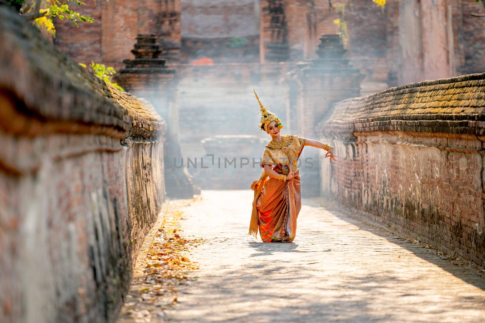Asian beautiful woman with traditional dress dance with different actions on the way to ancient building and smoke or mist in the background with day light.