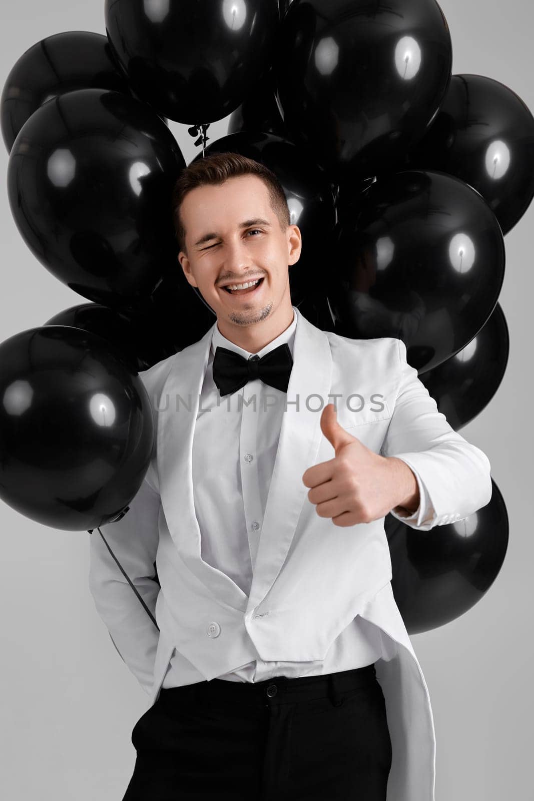 elegant caucasian man in white suit tuxedo with black air balloons on white background.
