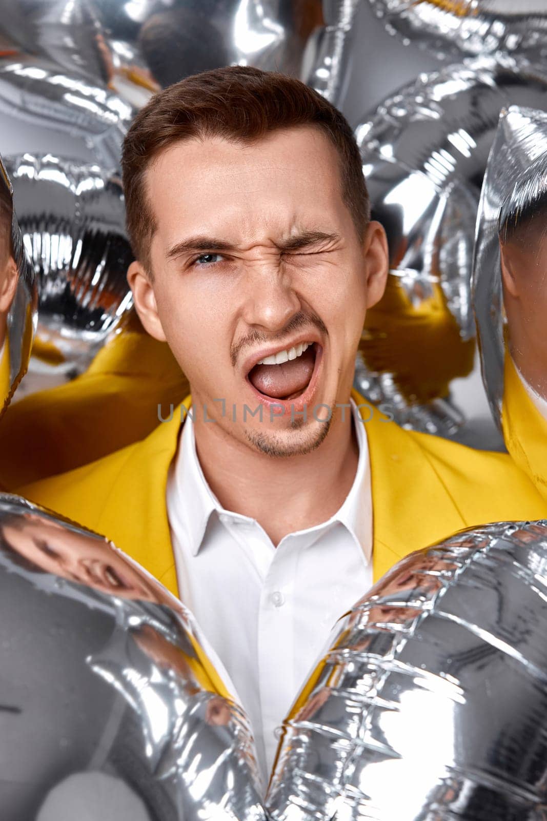 happy winking man in yellow jacket with a lot of silver air balloons. birthday party