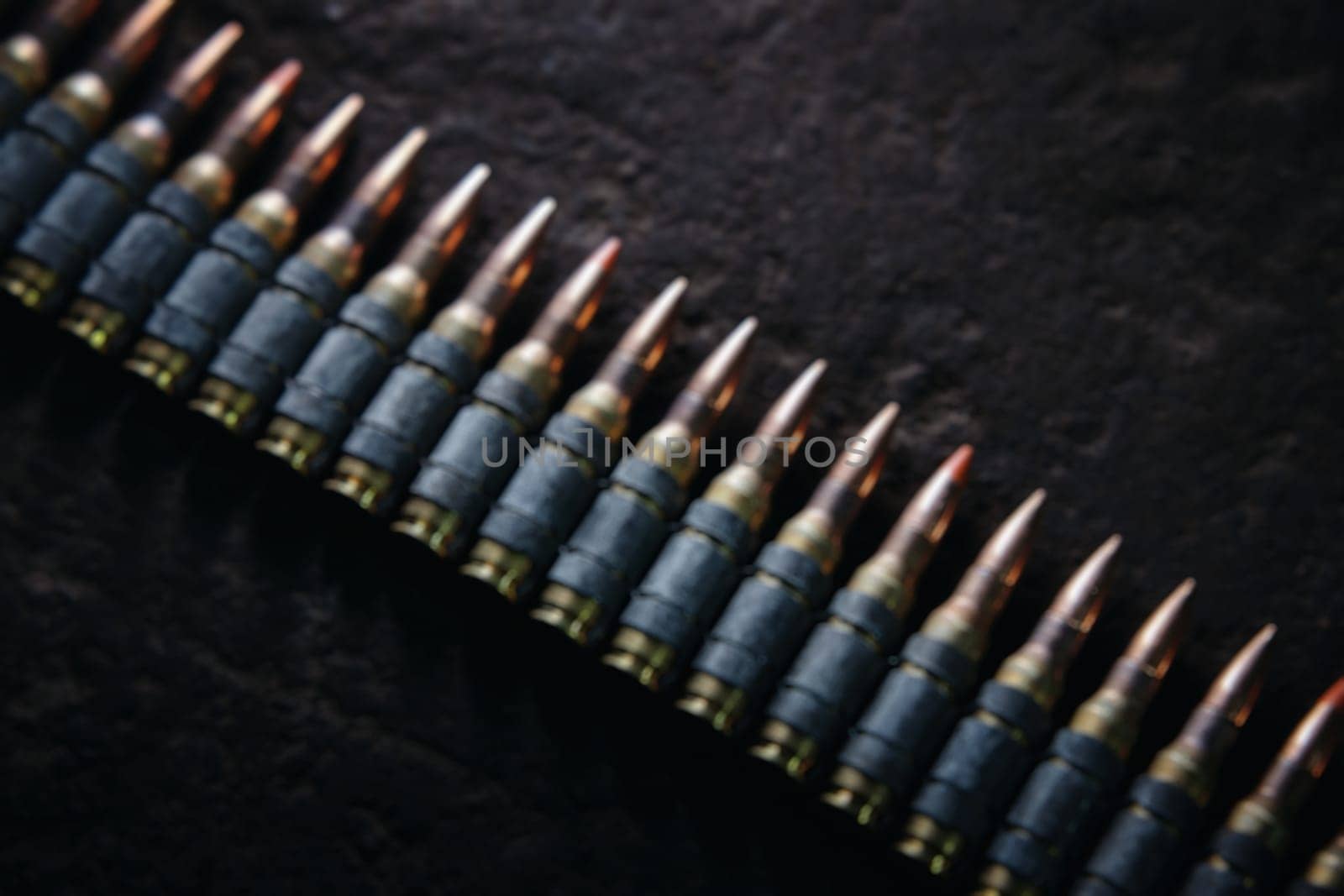 Machine gun bullet belt on the floor. Background on the military theme. Ammo, chain of ammo on concrete background. Top view of machine gun belt cartridge 7.62 mm caliber on dark blurred background by EvgeniyQW