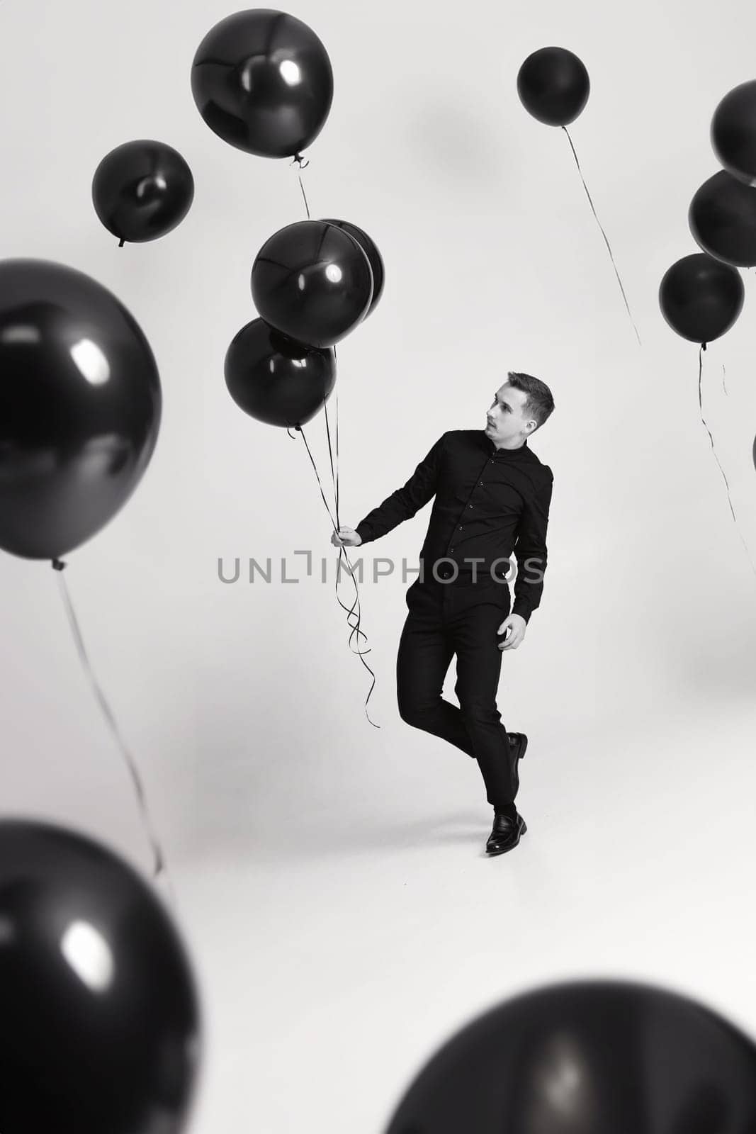 elegant caucasian man with bunch of black air balloons on white background. black and white