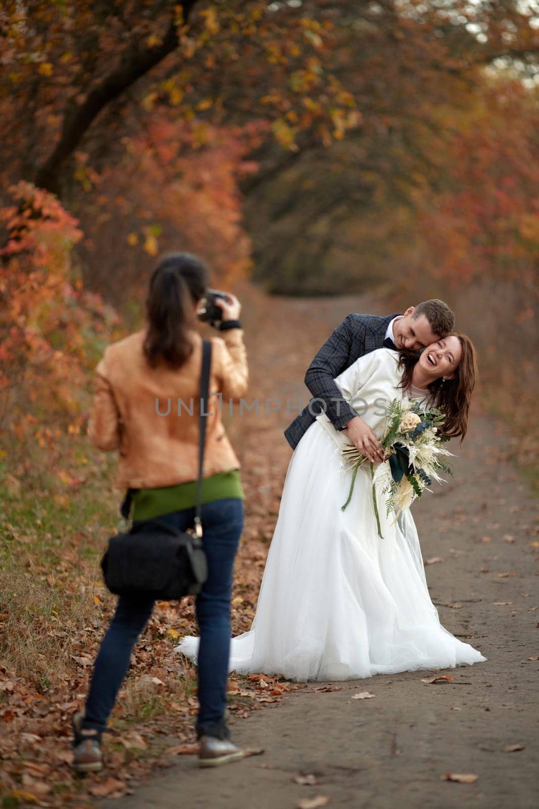 female wedding photographer taking pictures of the bride and groom in autumn