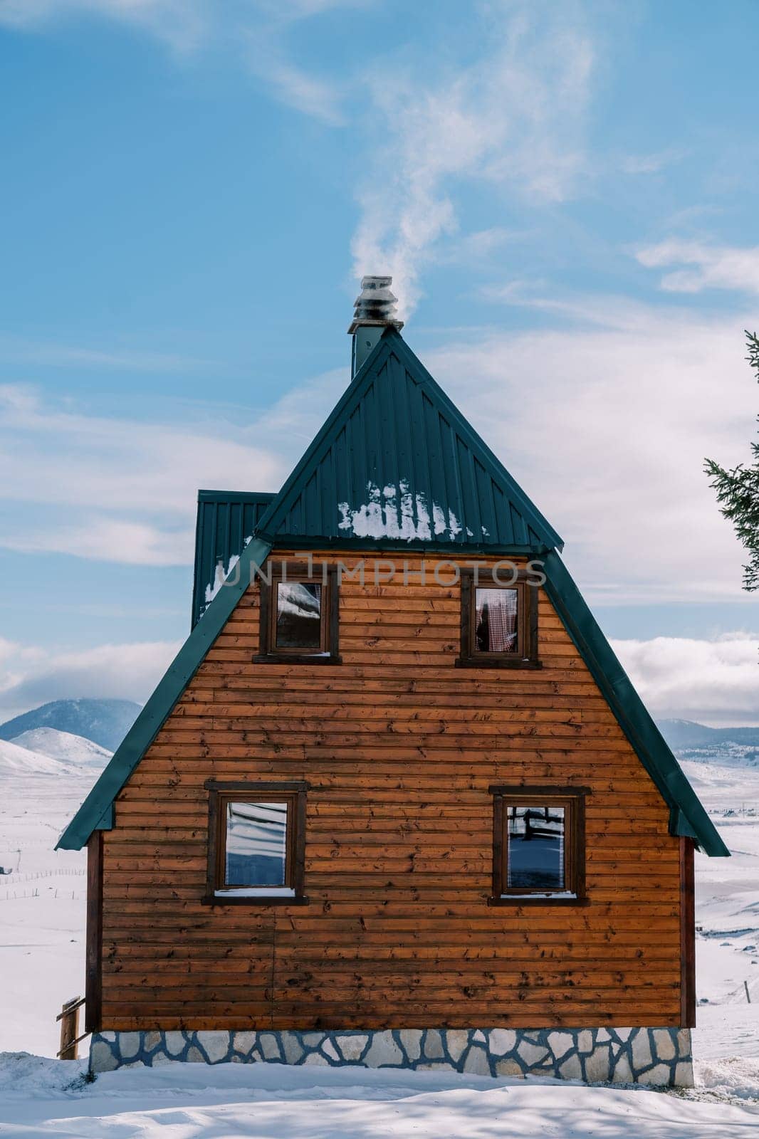 Smoke curls over the chimney of a two-story wooden cottage in a snowy village. High quality photo