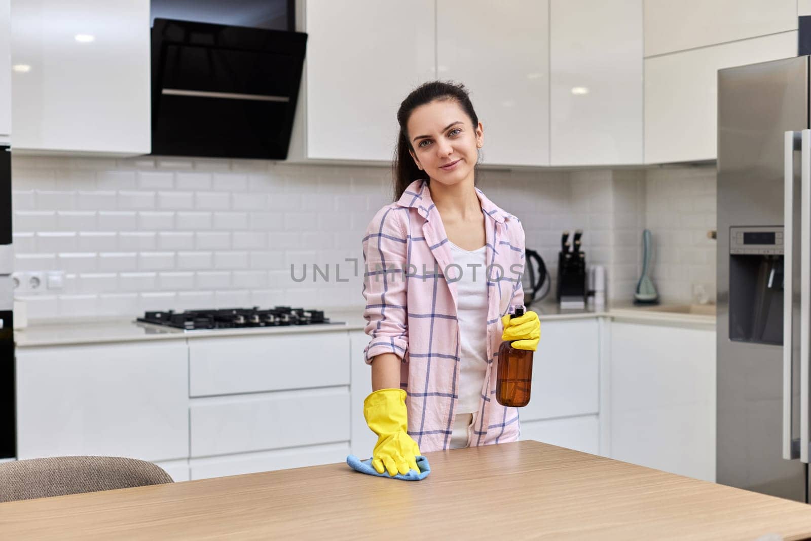 young woman in gloves smiling and cleaning table with microfiber cloth. chores at home. Housekeeping