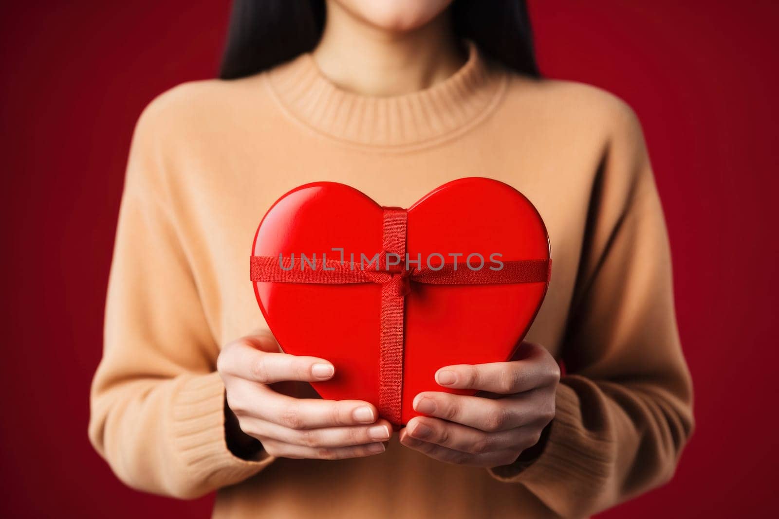 Woman's hands with a heart-shaped gift box against a red backdrop, ideal for an advertising poster, banner, or heartfelt greeting card