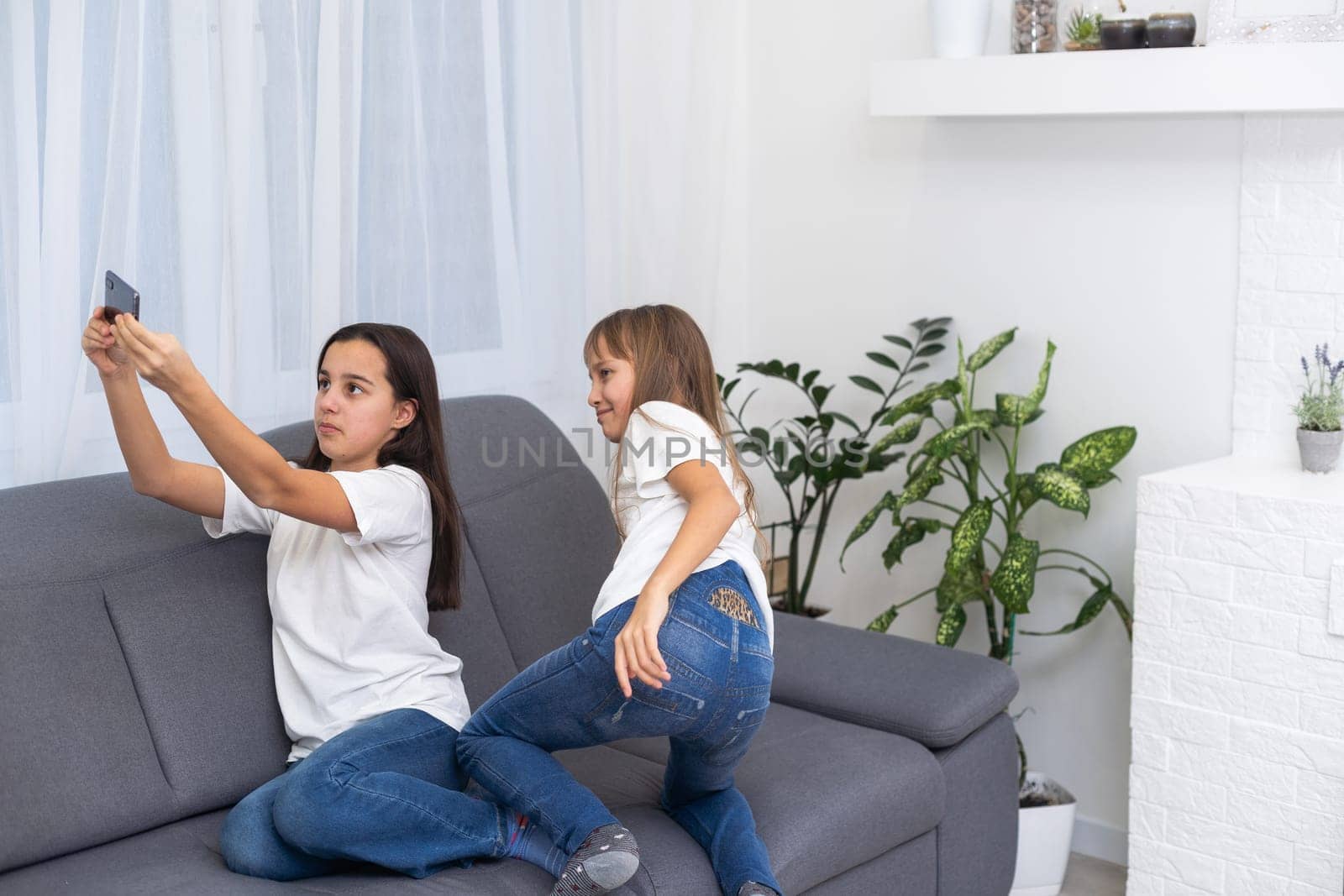 Child with smartphone at home. Two kids using smart phone, surfing internet or using social media. Two kids using online mobile phone, call, watching content, playing video games, sitting on couch by Andelov13