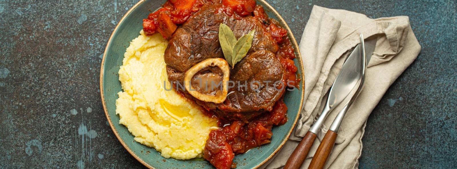 Traditional Italian dish Ossobuco all Milanese made with cut veal shank meat with vegetable tomato sauce served with corn polenta on ceramic plate top view on rustic stone background by its_al_dente