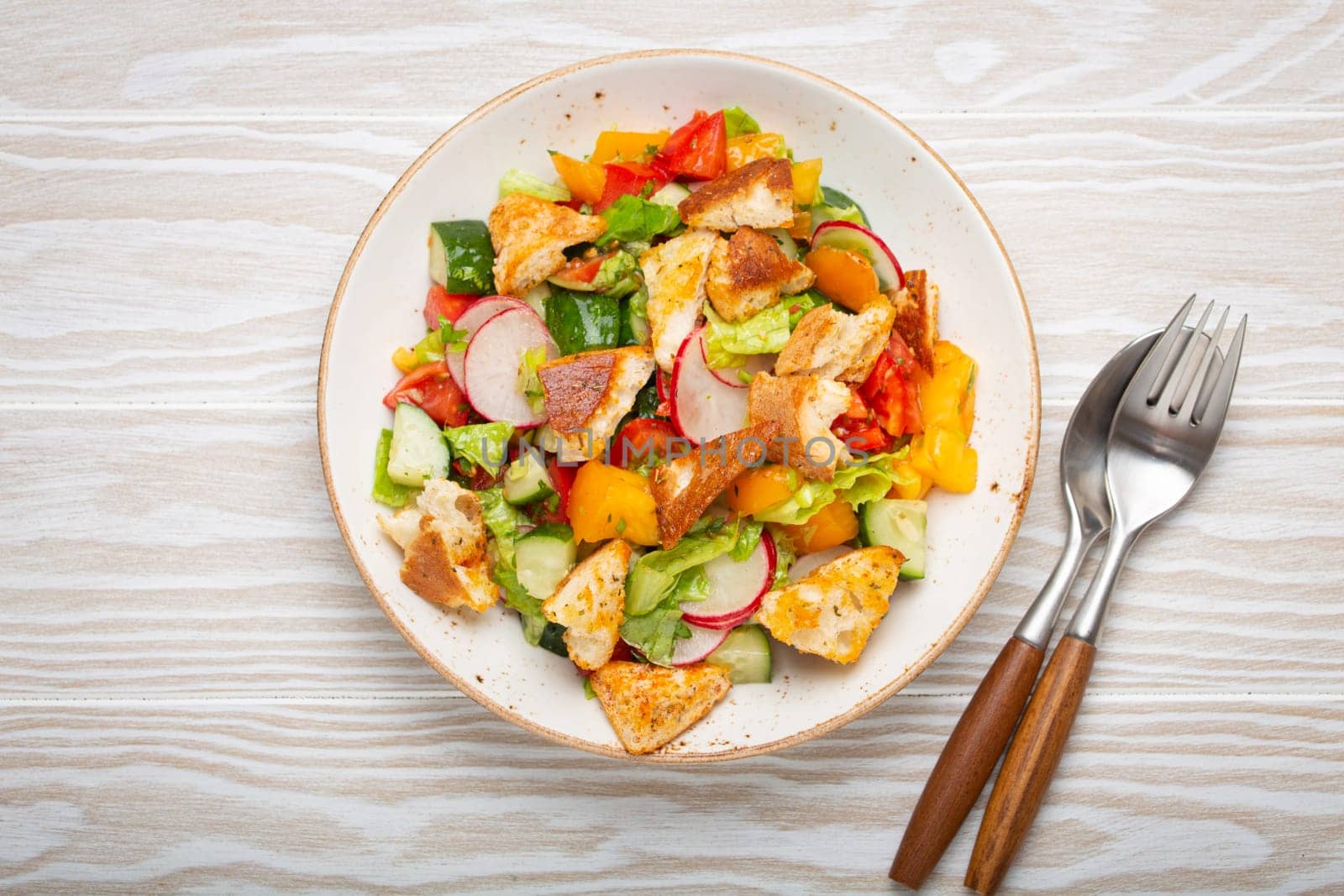 Traditional Levant dish Fattoush salad, Arab cuisine, with pita bread croutons, vegetables, herbs. Healthy Middle Eastern vegetarian salad, rustic wooden white background top view by its_al_dente
