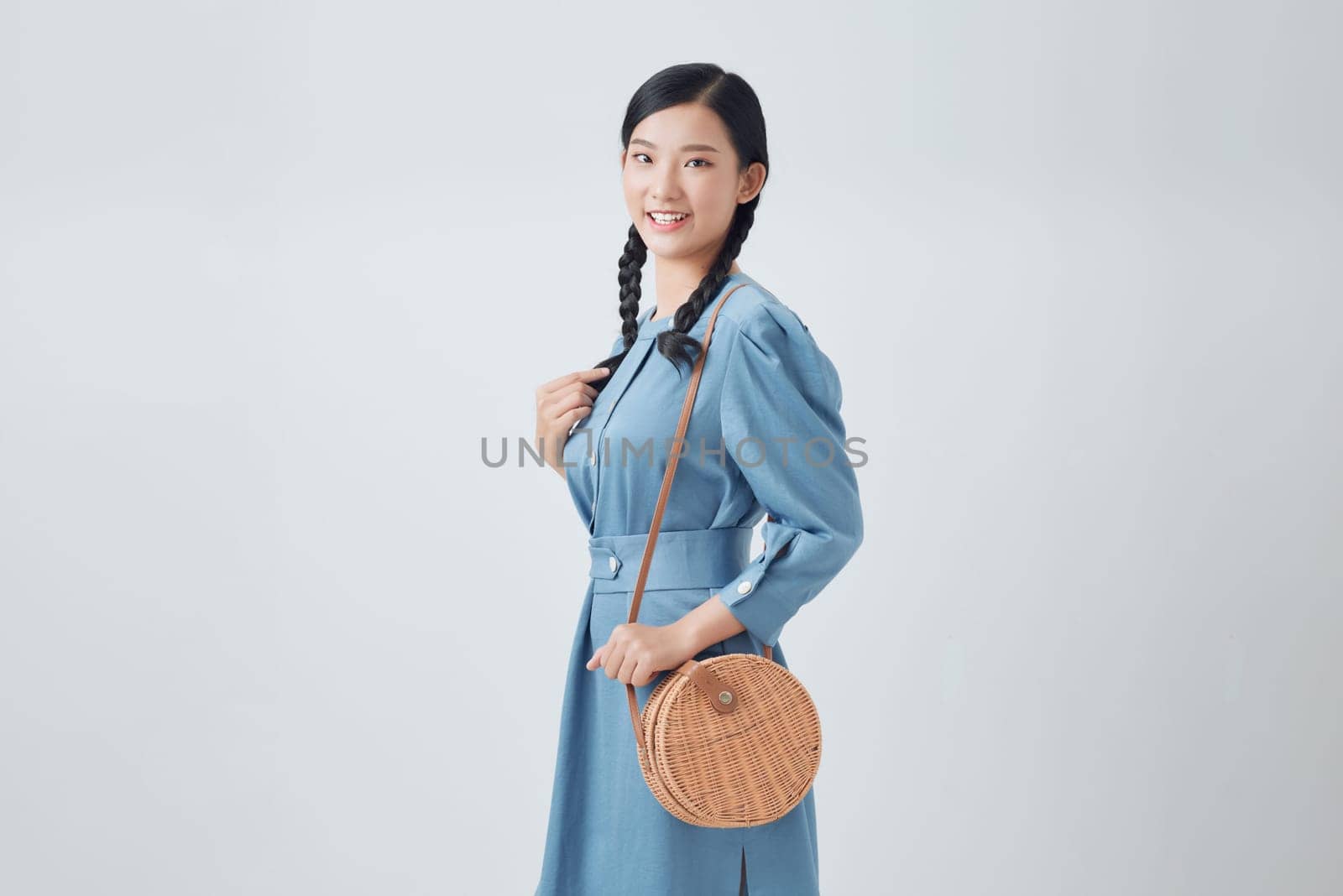 Elegant happy smiling woman wearing trendy denim dress, with small shoulder round wicker bag