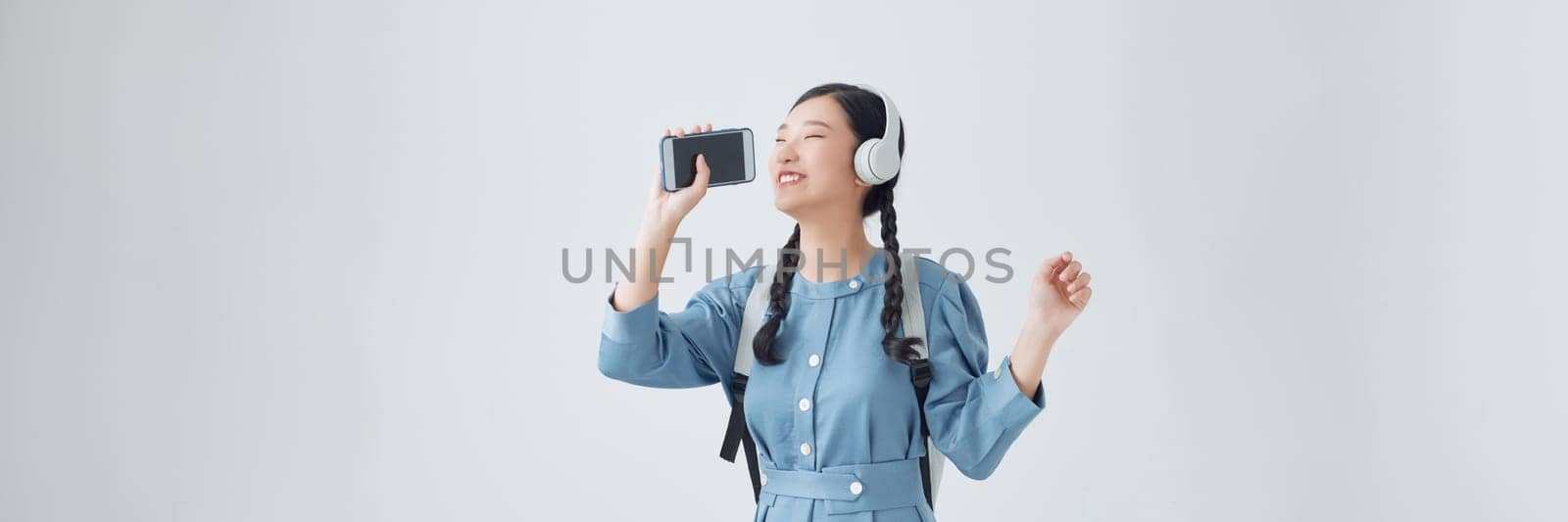  Beautiful young asian woman standing isolated, listening to music with headphones, singing