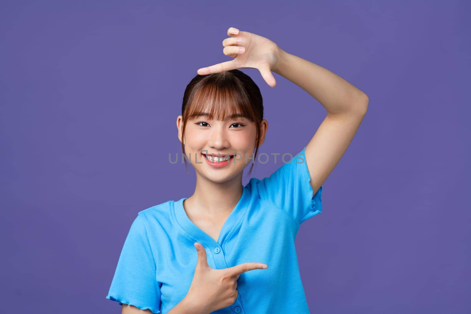 Beautiful young woman making frame with her fingers on purple background