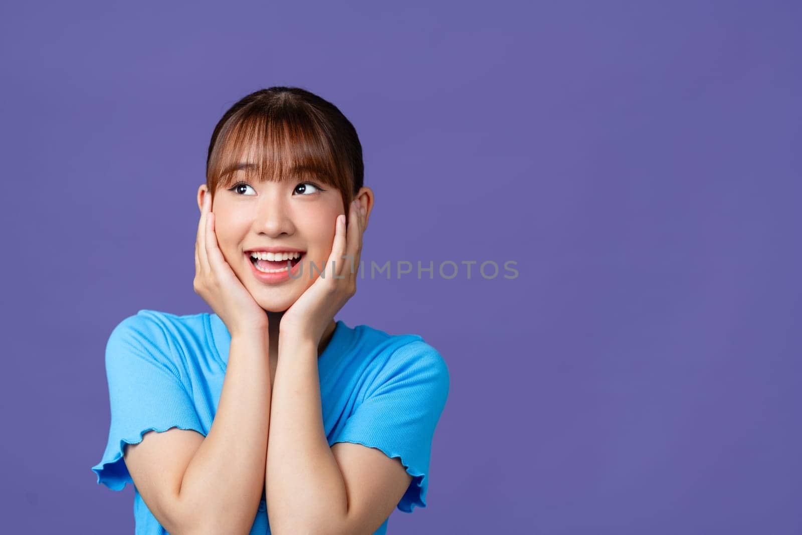 cute amazed girl holding head with two hands isolated on purple background