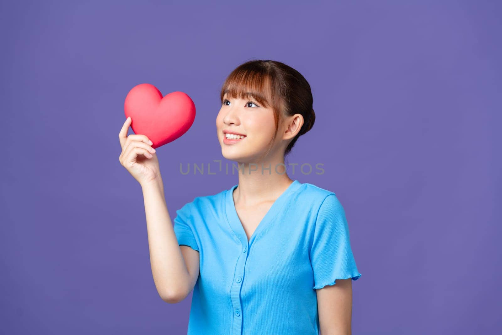 Smiling woman holding red heart on purple background by makidotvn