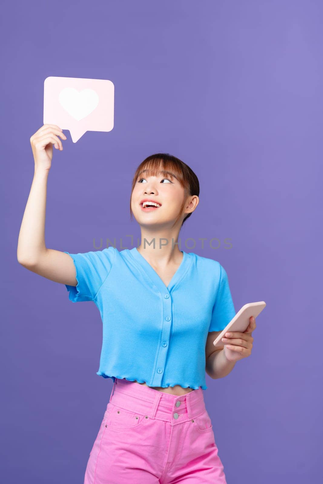 Young woman hold in hand use mobile cell phone heart form like icon sign on purple background