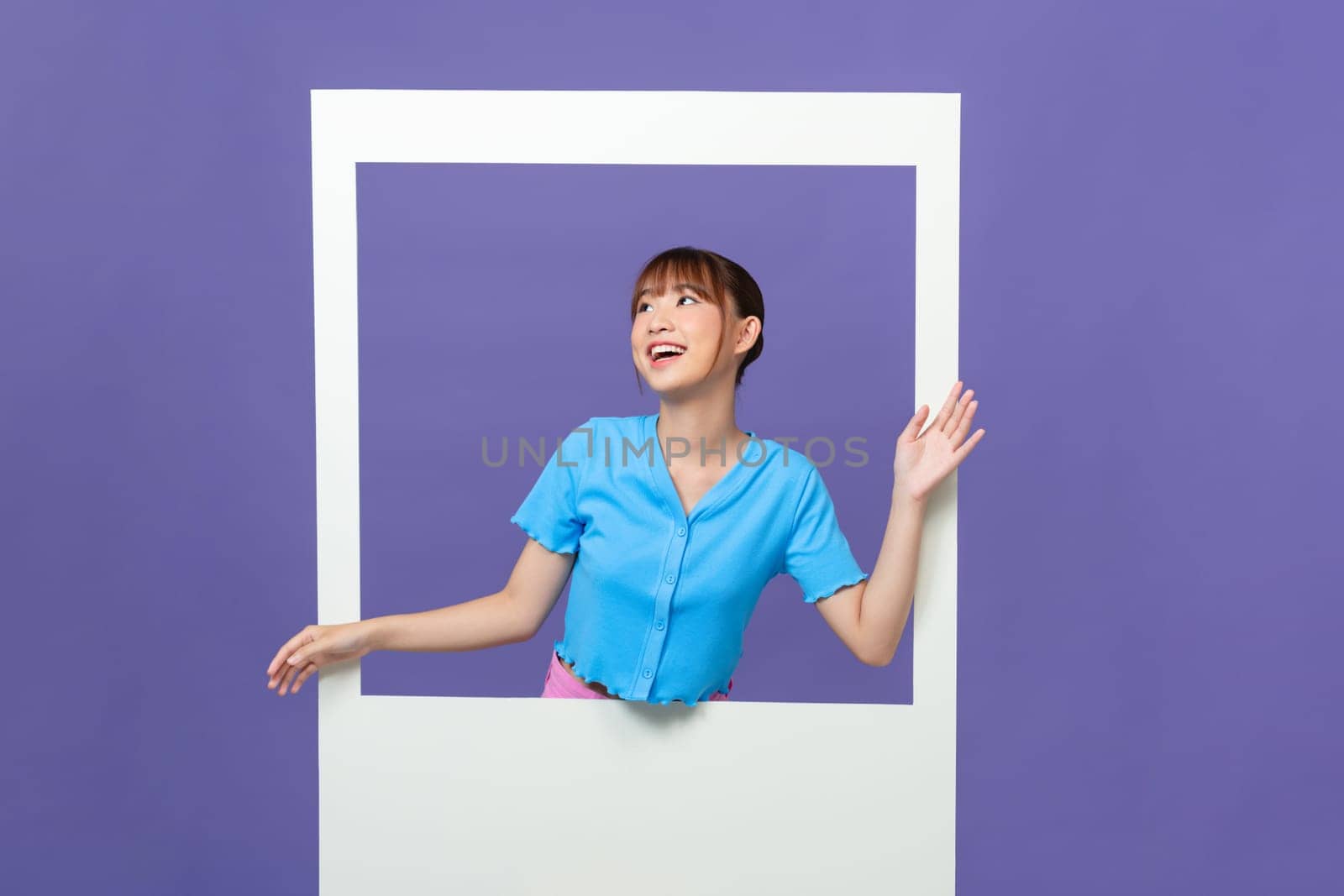 Photo of shiny funny young lady smiling looking through white window isolated on purple background