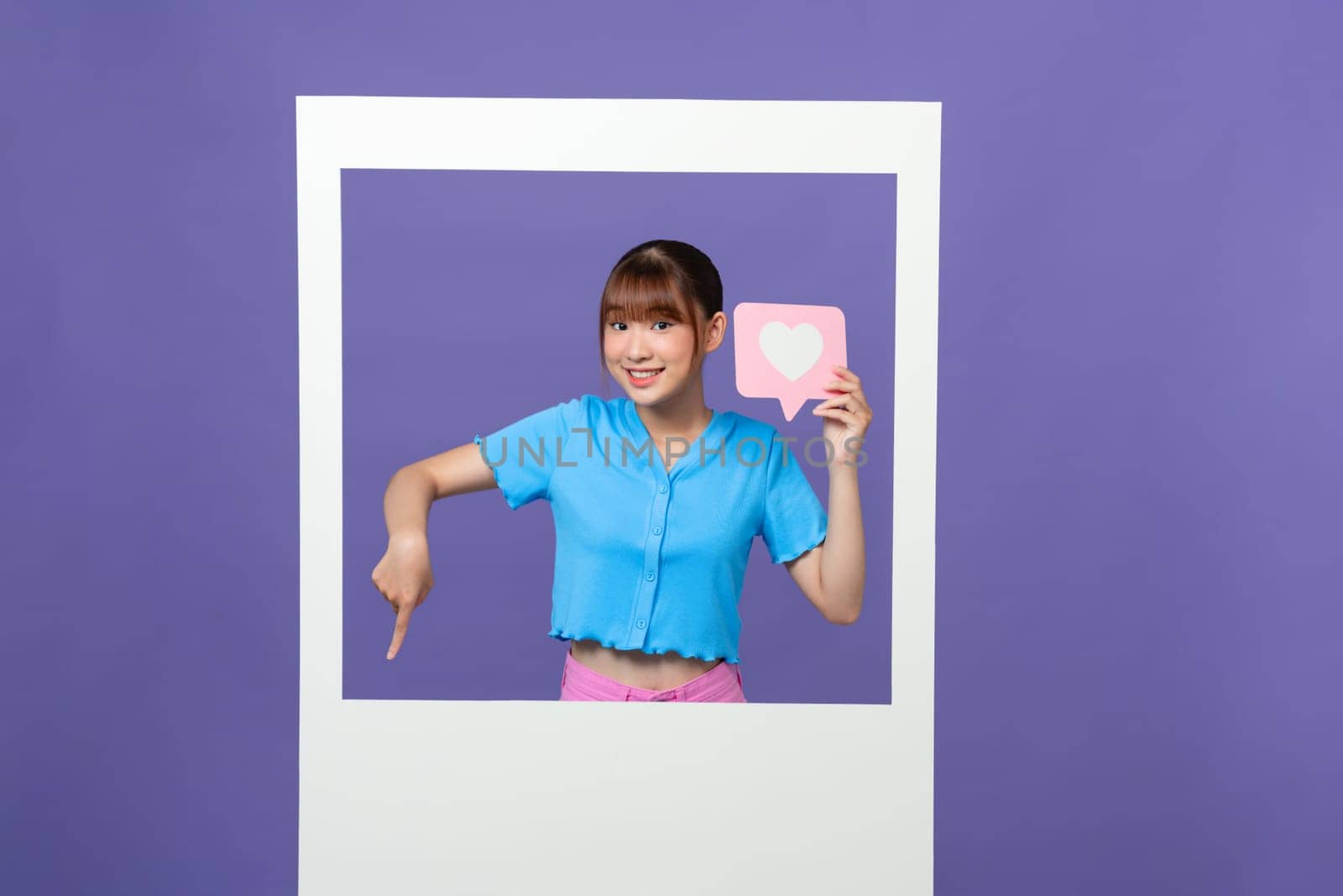 Charming excited lady in white frame point finger down follow subscribe isolated on purple background by makidotvn