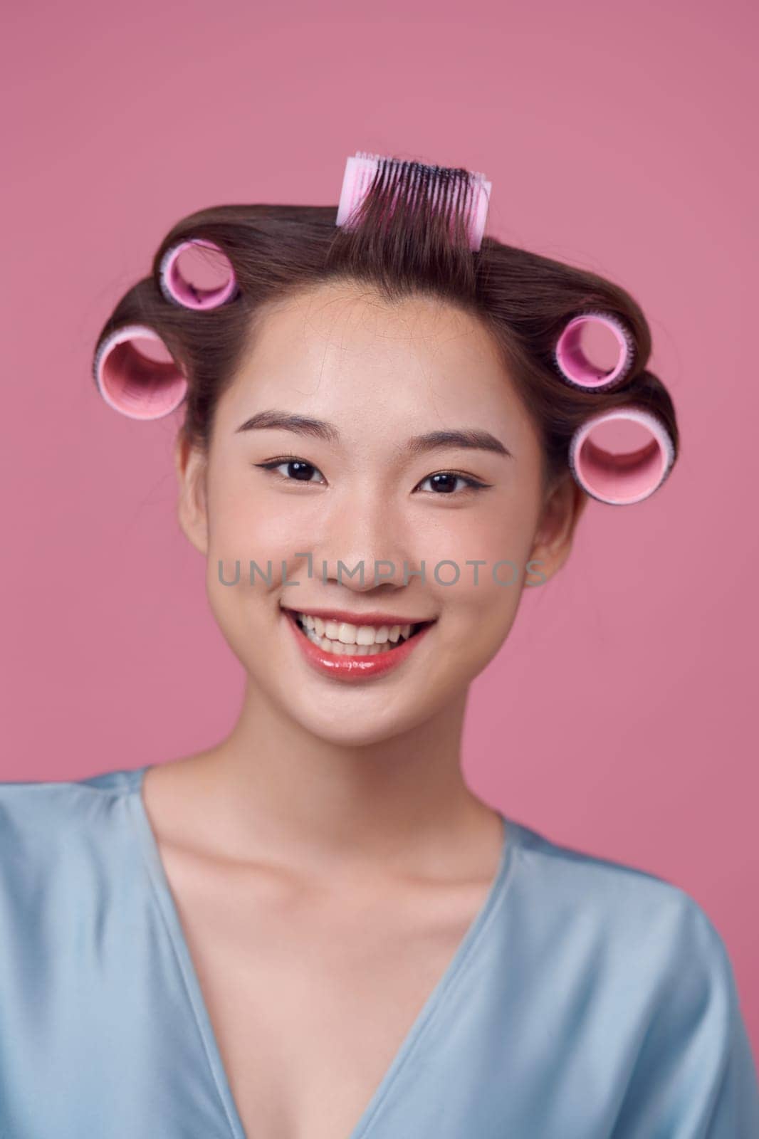 Beautiful girl in hair curlers on pink background.