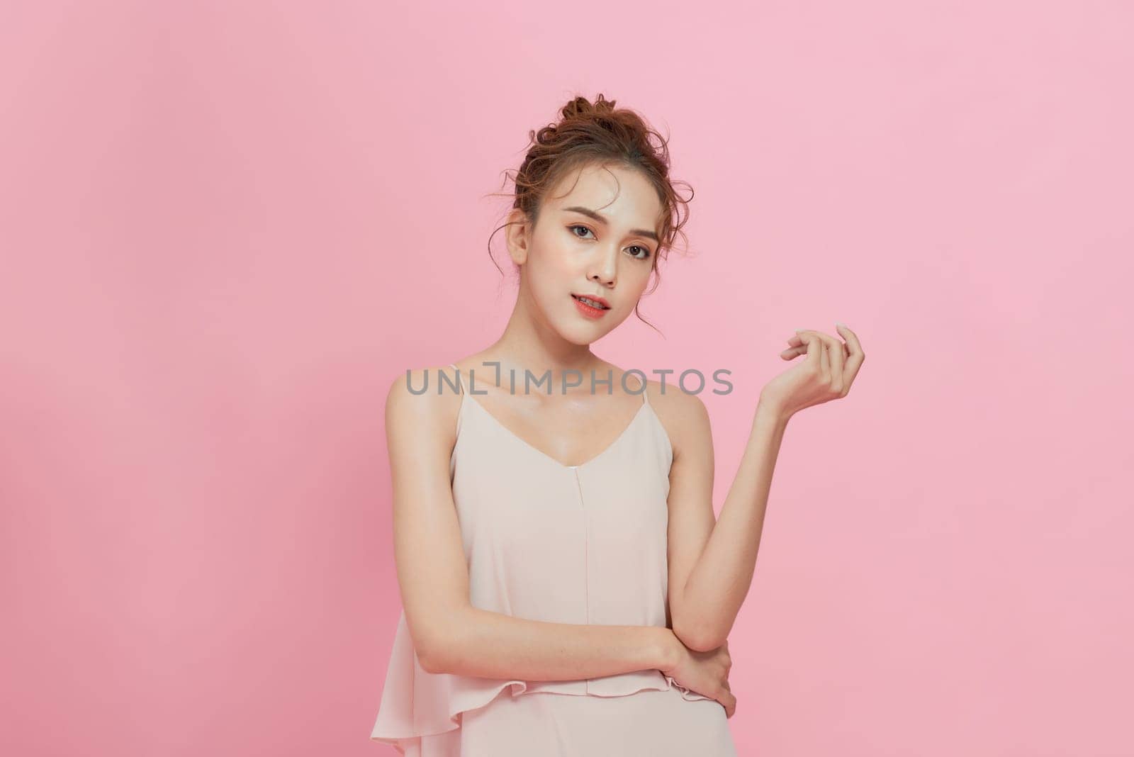 A smiling attractive woman in summer dress posing isolated over pink background