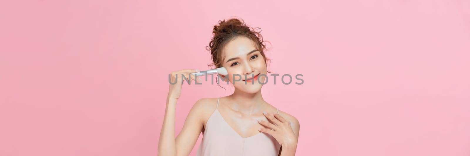 Woman applies powder on the face using makeup brush. by makidotvn