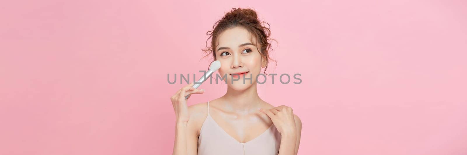 Portrait of a woman applying dry cosmetic tonal foundation on the face using makeup brush. by makidotvn
