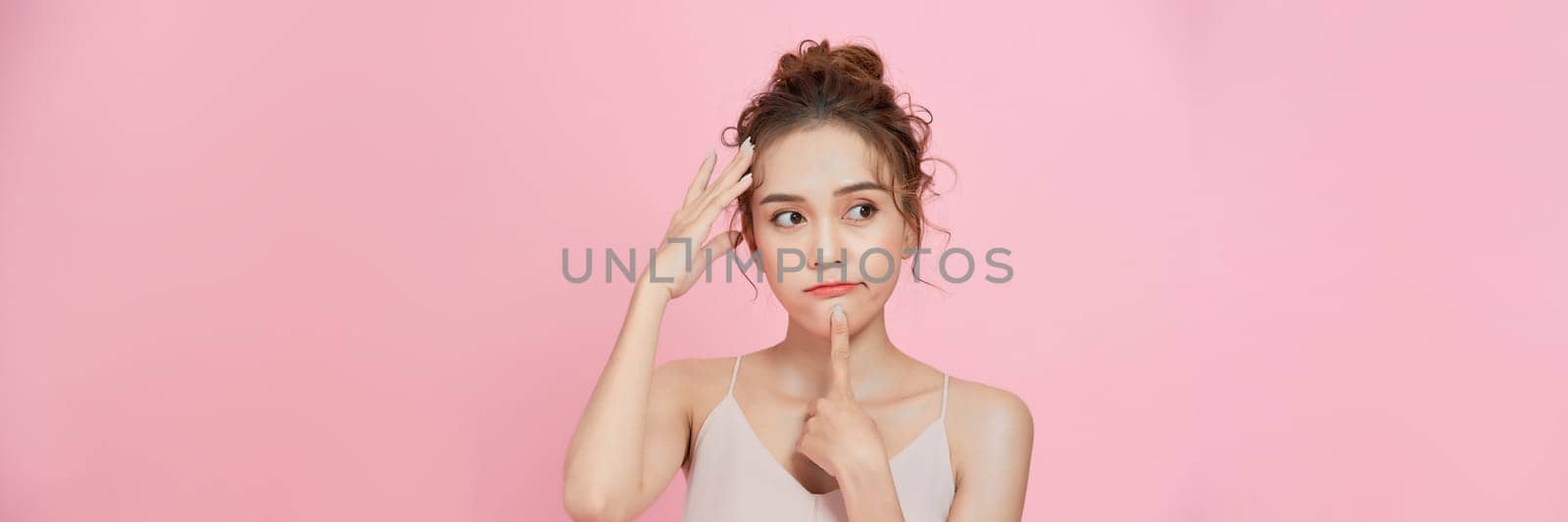 Portrait of a young woman thinking with finger on chin, isolated on pink background by makidotvn