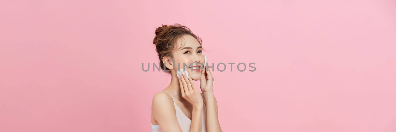 Woman removing makeup, holds cotton pads near face. 