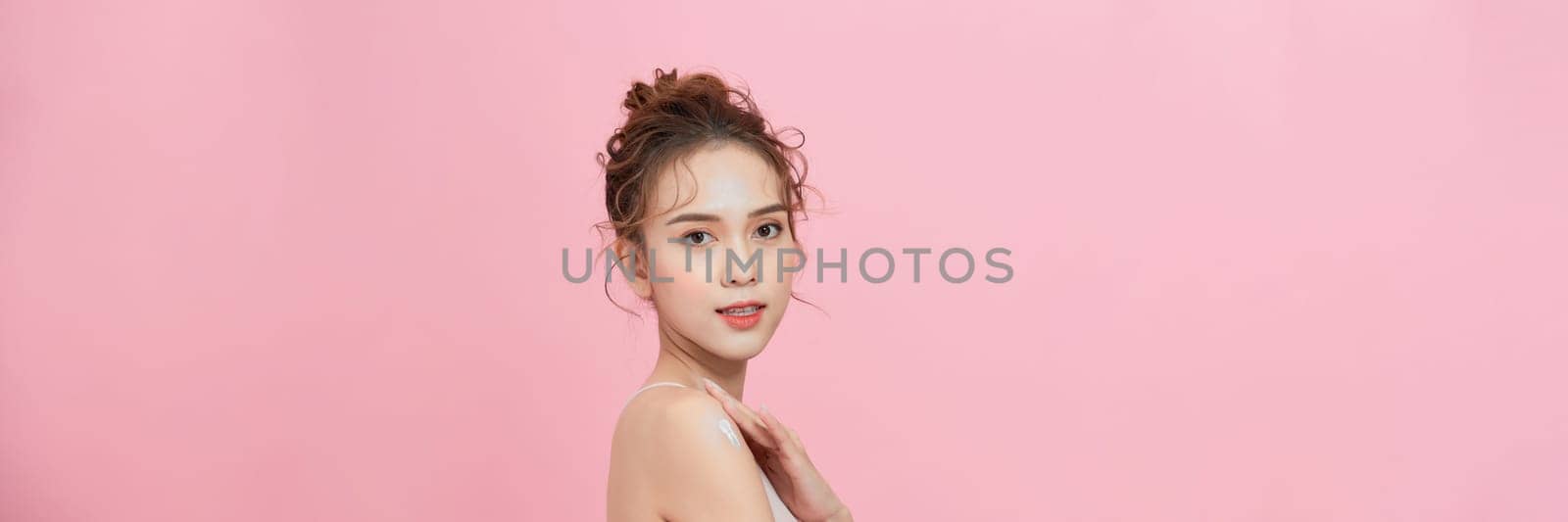 Woman applying body cream onto arm on pink background by makidotvn