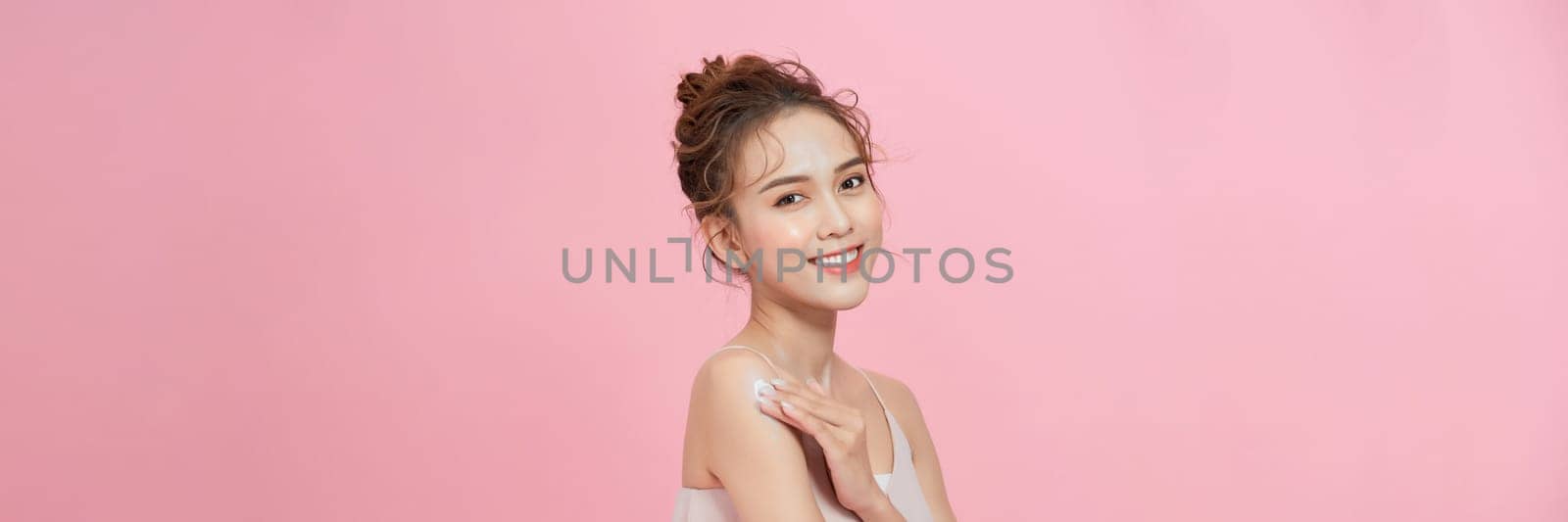 Young woman applying body cream onto shoulder on pink background by makidotvn