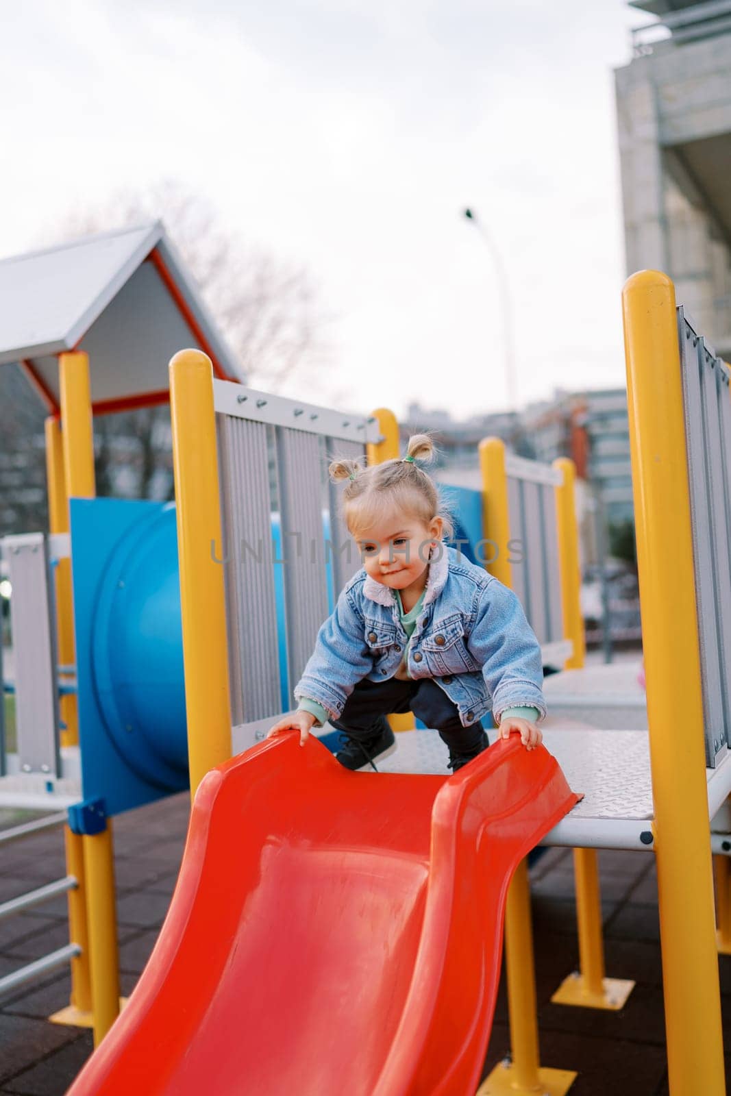 Little girl squatting on top of a slide holding onto the railings. High quality photo